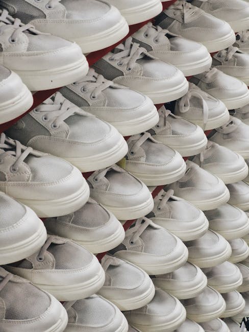 A close-up view of multiple white sneakers with grey accents arranged in neat rows on a retail display shelf, likely within a home or commercial shop environment. The shoes are positioned with their laces tied, and some are stacked slightly to show the side profile and toe box of each pair. The background suggests an indoor setting with even lighting, capturing the shoe material which appears to be a combination of leather and mesh. While the image primarily focuses on the footwear display, it exemplifies packing or organisation of personal items, relevant to household moving or packing processes that are part of home relocation services offered by Man with Van Hackney Marshes. The arrangement may be part of a packing stage during furniture transport or an inventory display in the context of moving logistics, aligned with the service category of removals.