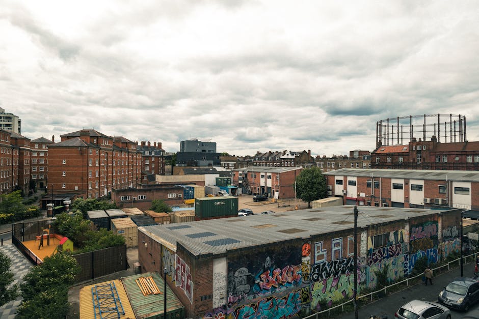 A wide view of an urban area showing a mix of residential and industrial buildings, with several multi-storey brick apartment blocks and warehouse-style structures. In the foreground, a rooftop with g